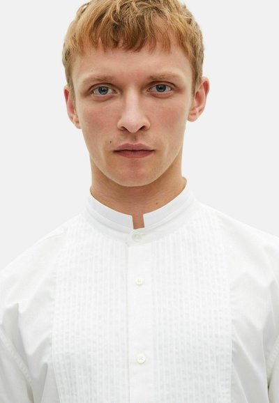 Witte shirt met een hoge kraag, verticale streeppatroon en subtiele knoopsluiting bij de nek, wat de minimalistische ontwerp benadrukt.