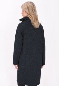 Cappotto lungo, blu scuro, realizzato in tessuto testurizzato. Presenta un colletto alto e una vestibilità ampia, con maniche leggermente svasate e tasche laterali.