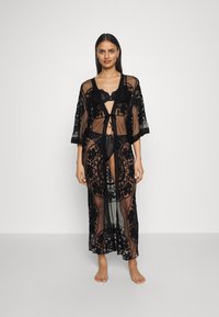 Czarny kimono w stylu szlafroka z koronką, ozdobiony kwiatowymi wzorami, wykonany z przezroczystej tkaniny, z szerokimi rękawami i wiązaniem w talii. Noszony na dopasowanej bieliźnie.