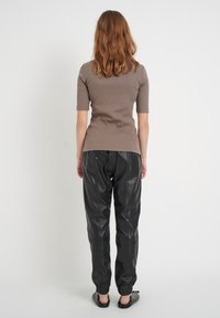 Krótki rękaw, dopasowana beżowa bluzka o prążkowanej fakturze, w połączeniu z czarnymi, skórzanymi joggerami z elastycznymi mankietami i bocznymi kieszeniami.