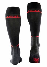 Calze nere lunghe fino al ginocchio con texture a coste, accenti rossi e logo "FALKE". Presentano un tallone e una punta rinforzati per durata e supporto.