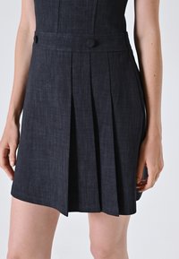 Dunkelblaudene Kleid mit einem taillierten Oberteil, einem gefalteten Rock, zwei Knöpfen an der Taille und einem Saum, der oberhalb des Knies endet.