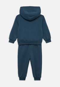 Μπλε ναυτικό βαμβακερό φόρμα που περιλαμβάνει μπλούζα με κουκούλα και παντελόνι με στενή εφαρμογή. Ριμπ μανσέτες και ζώνη μέσης με ομαλή, casual υφή.