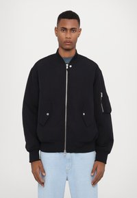 Black bomber jacket made of smooth fabric, features a zip front, two side pockets, and one zipped sleeve pocket. Ribbed cuffs and hem.
