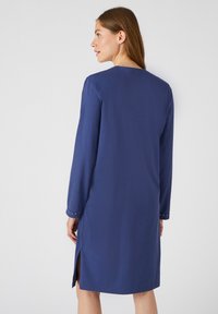 Abito lungo blu navy a maniche lunghe con taglio dritto, fessure laterali e dettagli con borchie sui polsini. Tessuto liscio con scollatura modesta.