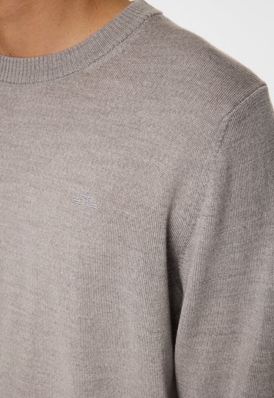 Harmaa neulepaita, jossa on pyöreä pääntie ja hillitty logotyyppi. Pehmeä rakenne, jossa on vahvistetut kaula-aukko ja hihansuut.