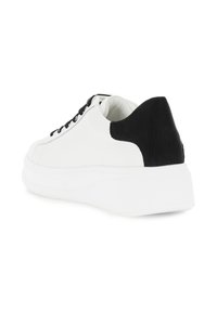 Valkoinen tennari paksulla pohjalla, mustalla uritetulla kantapaneelilla ja mustilla nauhoilla, kulmassa, jotta selkä- ja sivuprofiili näkyvät valkoista taustaa vasten.