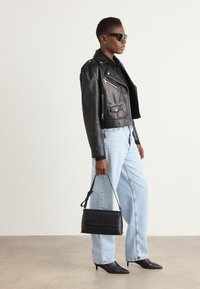 Svart skinnmotorjakke, lyseblå denimjeans, svarte spisse hæler og en svart håndveske. Har sølvglidelåsdetaljer og en kort design.