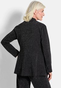 Zwarte fitted jas van een textiel met een gestructureerde stof met zilveren stippen. Lange mouwen en een ronde onderrand verbeteren het op maat gemaakte ontwerp.