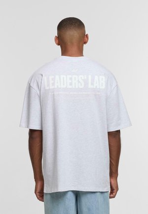 Gray cotton t-shirt with short sleeves. Large text on the back reads "LEADERS' LAB" in white. Relaxed fit, slightly dropped shoulder seam.