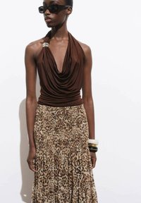 Hnědý halter top s volně drapenou tkaninou přes sukni s leopardím potiskem, která má sklady a vrstvený design. Obsahuje odvážné náramky.