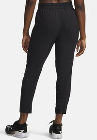 Zwarte sportbroek met een elastische tailleband, taps toelopende pasvorm, ritsen bij de enkels en een gladde textuur, gecombineerd met zwarte sportschoenen.