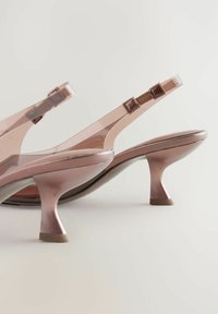 Vaaleanpunaiset läpinäkyvät korkokengät, joissa on kiiltävä pinta, ohut hihna ja ainutlaatuinen levenevä korko. Lämminsävyinen pinta ja minimalistinen tyyli.
