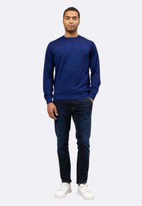 Maglione blu navy a collo rotondo in un morbido filato, abbinato a jeans scuri e sneaker bianche. La vestibilità è casual, ideale per l'uso quotidiano.