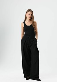 Débardeur côtelé noir associé à un pantalon noir taille haute, jambe large. Le pantalon présente des plis et une passants de ceinture avant avec un anneau argenté.