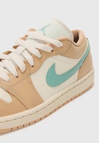 Baskets beige et crème avec un Swoosh Nike bleu clair, en cuir et textile, comportant des lacets blancs et une semelle texturée.