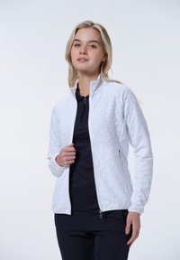 Weiße Zip-Jacke mit strukturiertem Blumenmuster, hohem Kragen und zwei Seitentaschen, über einem dunkelblauen Oberteil getragen, mit enganliegenden Ärmeln.