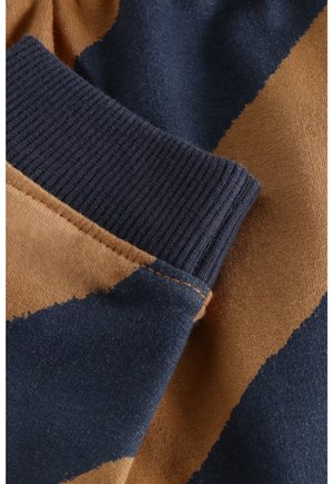 Close-up van een kledingmouw met geribbelde manchetten in donkerblauw en bruin gekleurd gebreid stof.