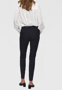 Biała bluzka z lejącym materiałem, czarne spodnie slim-fit oraz czarne buty na słupku. Miękka tekstura, prosty krój i klasyczne kolory.