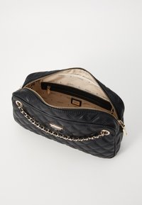 Borsa crossbody in pelle nera trapuntata con tracolla in oro e chiusura con zip. L'interno foderato presenta una stampa con il marchio e una tasca con zip.