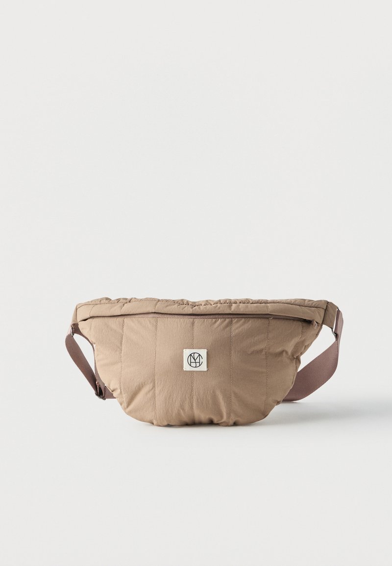 Μπεζ επενδυμένη τσάντα μέσης με κλείσιμο φερμουάρ και ρυθμιζόμενο καφέ λουράκι, με μικρό άσπρο λογότυπο στη μπροστινή μέση.