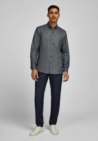 Donkerblauw overhemd met knopen, van een gestructureerde stof, lange mouwen en een kraag, gecombineerd met donkere spijkerbroeken en witte sneakers.