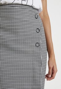 Svart och vit houndstooth kjol med hög midja, med tre runda svarta knappar fram och en mjuk textur.