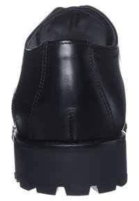 Chaussure en cuir noir avec un dos arrondi, semelle épaisse et texturée, et des détails de couture visibles. Le talon est robuste et légèrement surélevé.