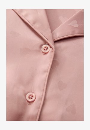 Lichtroze pyjamashirt van soepel materiaal, met een subtiel hartjespatroon, een notch-kraag en twee knopen aan de voorkant.