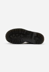 Semelle de botte noire avec des crampons profonds et des bandes de roulement, présentant des motifs rectangulaires et en forme d'étoile pour une meilleure adhérence sur un fond blanc.