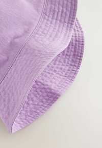 Chapeau seau violet en tissu doux, avec une texture lisse, des coutures le long du bord, et une forme de couronne arrondie.