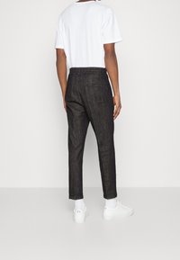 Mörka denimbyxor med tapered fit, elastisk midja och en bakficka, i kombination med en enkel vit t-shirt och vita sneakers.