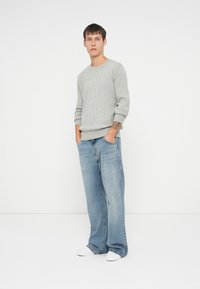 Svijetlosiva rebrasta pletena dukserica s dugim rukavima, uparena sa svijetloplavim širokim trapericama i bijelim natikačama. Jednostavan, ležeran outfit.