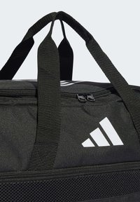 Black duffel bag with double top handles, zip closure, and a mesh side pocket. Features a white logo. Durable fabric material with textured finish.