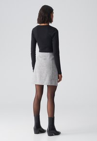 Schwarzes, kurzes Langarmoberteil, kombiniert mit einem grauen, strukturierten Minirock mit Seitentasche, schwarzen blickdichten Strumpfhosen und klobigen Stiefeletten.