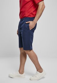 Marineblauwe shorts van zachte stof, met een verstelbare tailleband, zijzakken en een relaxte pasvorm, gecombineerd met witte sneakers.