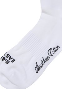 Calzino bianco in cotone con dettagli a coste. Presenta un testo nero con le scritte "Another Action" e "8-9.5" che indica la misura. Texture liscia, design alla caviglia.