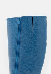 Bottine bleue en matière synthétique texturée, dotée d'une fermeture éclair latérale et d'un design élégant avec un motif peau de crocodile.