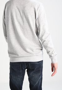 Sudadera gris de algodón con cuello redondo, manga larga, puños y bajo acanalados, combinada con jeans de mezclilla azul oscuro con bolsillos traseros.