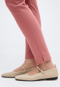 Μπεζ μπαλαρίνες Mary Jane με μυτερή μύτη και λουράκια με αγκράφα, συνδυασμένες με ροζ παντελόνια cropped με πλαϊνές σχισμές στους αστραγάλους.