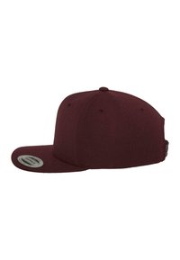 Bordó snapback sapka lapos ernyővel, texturált anyagból, oldalán szellőzőlyukakkal, és egy kör alakú címkével az ernyőn.
