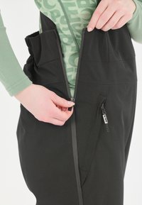 Schwarze Außenhose mit einem Frontreißverschluss und einer Seitentasche mit Reißverschluss. Der Stoff wirkt wasserabweisend und hat eine glatte Textur.