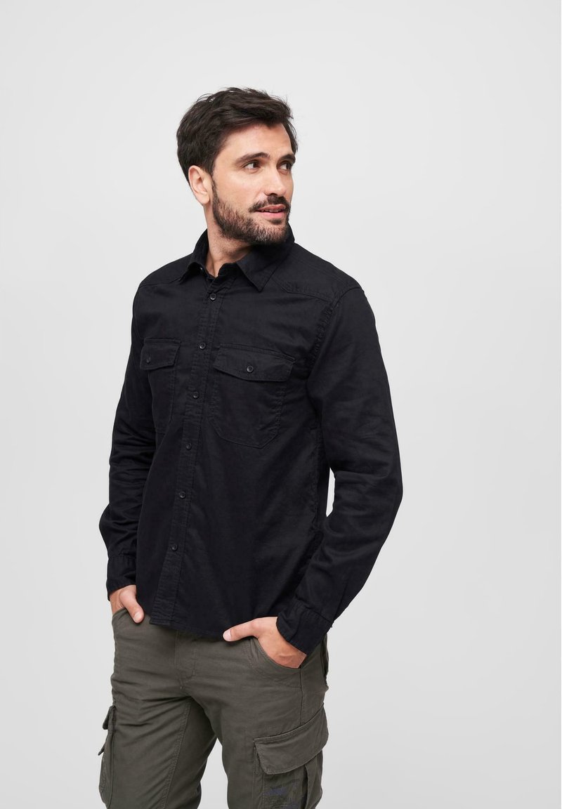 Black button-up shirt with two chest pockets, cotton fabric, long sleeves, lightweight texture, paired with olive cargo pants.