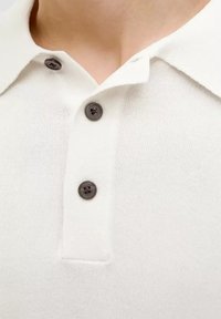 Bílá polo košile vyrobená z měkké tkaniny, s klasickým límečkem a třemi tmavě hnědými knoflíky na léze. Hladká textura a čistý design.