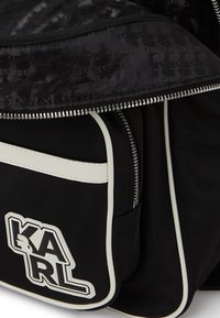Črna tkaninska torba z belimi detajli, z zadrgo in logotipom KARL. Zasnova z reliefno notranjostjo in elegantno, strukturirano obliko.