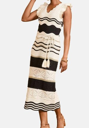Femme portant une robe midi tricotée sans manches rayée noir et crème avec un motif texturé et une ceinture nouée à la taille.