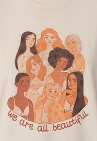 Krémové tričko s grafikou osmi různorodých žen s různými účesy a odstíny pleti, s textem "všechny jsme krásné" v hnědé barvě.