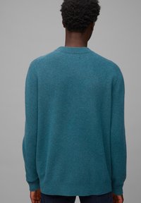 Tyrkysový pletený svetr s kulatým výstřihem, dlouhými rukávy a volným střihem, vyrobený z měkkého texturovaného materiálu. Zadní pohled ukazuje jemný vzor.