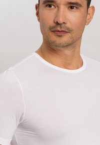 Hedvábný bílý tričko s krátkým rukávem z lehké bavlněné směsi. Hladká textura s přiléhavým střihem, krátkými rukávy a minimálním množstvím švů.