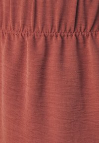 Kankaan ruskea väri, jossa on teksturoitu pinta, varustettuna kerätystä elastisesta vyötäröstä ja pehmeästä, hieman rypistyneestä ulkonäöstä.